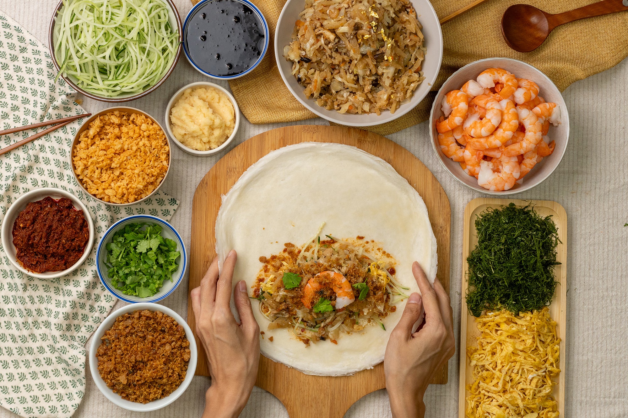 Preparing a golden popiah set with fresh ingredients, including shrimp, vegetables, and various toppings on a wooden board.