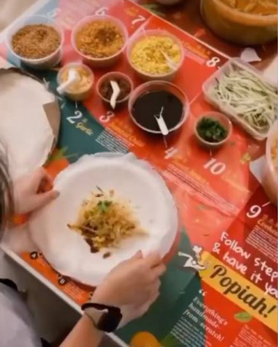 Child rolling popiah at home on a Fortune Food step-by-step popiah placemat, with fillings and sauces laid out
