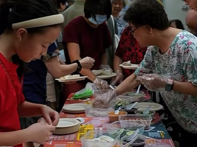 Colleagues rolling their own popiah along a table of placemats, fillings and condiments