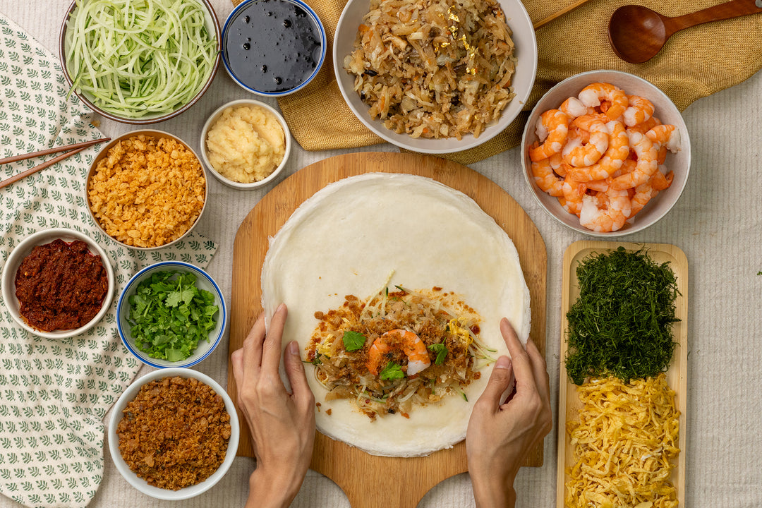 Preparing a golden popiah set with fresh ingredients, including shrimp, vegetables, and various toppings on a wooden board.